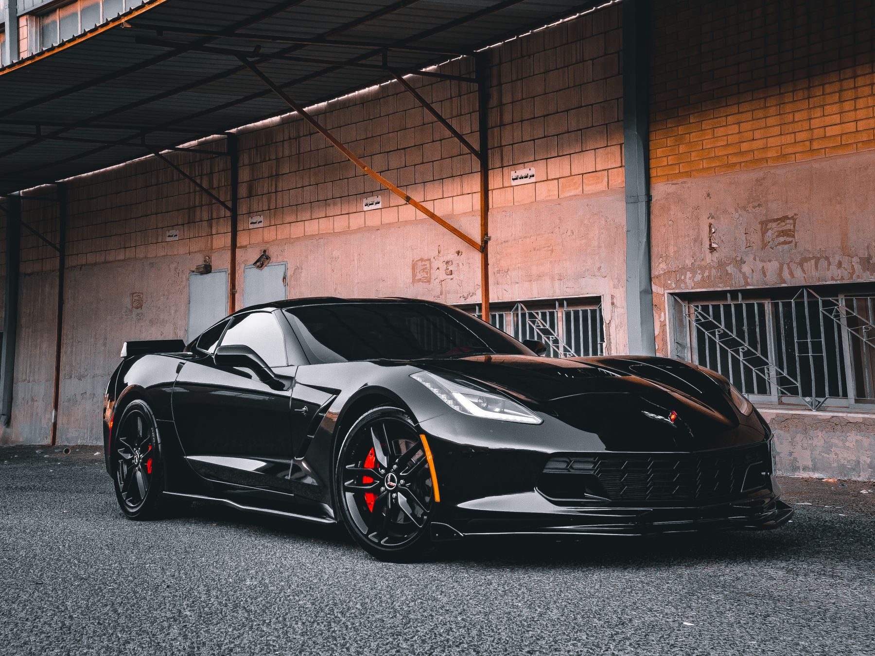 A glossy black sports car with red brake calipers parked in a concrete detailing bay, its paintwork mirror-reflecting the surroundings.